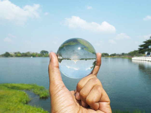 Mano sostiene esfera, lago y cielo reflejados.